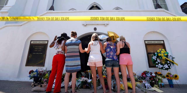 FILE- In this June 18, 2015, file photo, a group of women pray together at a makeshift memorial on the sidewalk in front of the Emanuel AME Church in Charleston, S.C. A single gunman shot and killed several people, including the pastor, at a prayer meeting inside the historic black church. In a poll conducted by the Associated Press and the Times Square Alliance found the most important news events to Americans in the past year were the shootings in Charleston, San Bernardino, Calif., Oregon and Tennessee. (AP Photo/Stephen B. Morton, File)