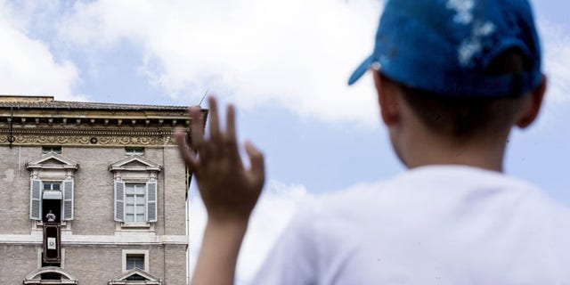 A young boy waves as Pope Francis delivers his message from his studio window overlooking St. Peter's Square during the Sunday Angelus prayer, at the Vatican, Sunday, Aug. 14, 2016. (Angelo Carconi/ANSA via AP)