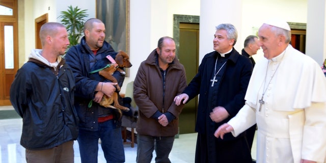 In this picture provided by the Vatican newspaper L'Osservatore Romano, Pope Francis, right, is flanked by Vatican Almoner Archbishop Konrad Krajewski as he welcomes four men at the Vatican, Tuesday, Dec. 17, 2013. Four homeless people, one of them bringing his dog, helped Pope Francis celebrate his 77th birthday at the Vatican Tuesday. They live on the street in the Rome neighborhood just outside the Holy See's walls and were invited by the Vatican official in charge of alms-giving to attend the morning Mass which Francis celebrates daily at the hotel where he lives on Vatican City grounds, the Vatican said. One of the men held his dog as he was presented to Francis after the guests chatted following Mass. The Vatican also said Francis invited his household help to join him in a "family-like" atmosphere, and he spoke of them one by one during his homily. (AP Photo/L'Osservatore Romano)