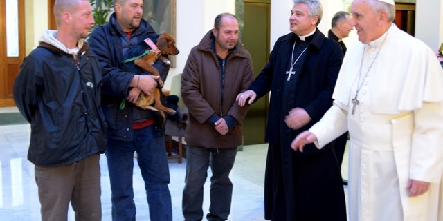 In this picture provided by the Vatican newspaper L'Osservatore Romano, Pope Francis, right, is flanked by Vatican Almoner Archbishop Konrad Krajewski as he welcomes four men at the Vatican, Tuesday, Dec. 17, 2013. Four homeless people, one of them bringing his dog, helped Pope Francis celebrate his 77th birthday at the Vatican Tuesday. They live on the street in the Rome neighborhood just outside the Holy See's walls and were invited by the Vatican official in charge of alms-giving to attend the morning Mass which Francis celebrates daily at the hotel where he lives on Vatican City grounds, the Vatican said. One of the men held his dog as he was presented to Francis after the guests chatted following Mass. The Vatican also said Francis invited his household help to join him in a "family-like" atmosphere, and he spoke of them one by one during his homily. (AP Photo/L'Osservatore Romano)