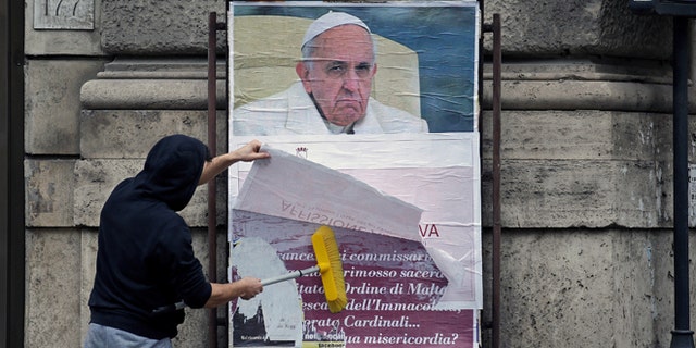 A worker covers a poster accusing the pope of attacking conservative Catholics in Rome, Italy, February 5, 2017