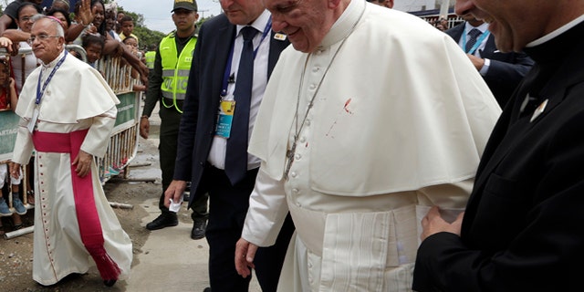 A small drop of blood stains Pope Francis' white cassock as he is helped by a priest, after knocking his head on the popemobile in Cartagena, Colombia, Sunday, Sept. 10, 2017.
