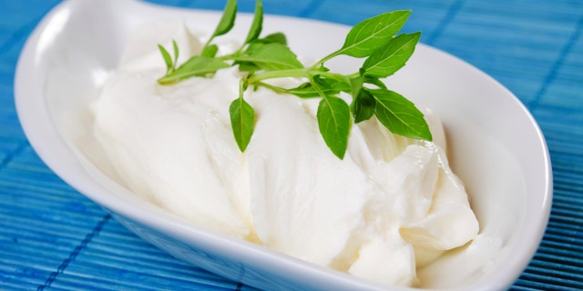 Sour cream with basil leaves on blue background