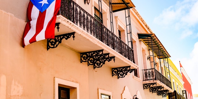 Colorful house facades along a street in Old San Juan, Puerto Rico with a Puerto Rican flag hanging down from one of the balconies