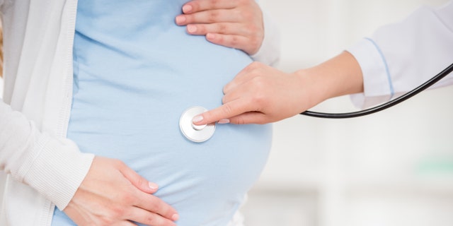 Close-up of doctor checking pregnant woman's tummy with stethoscope.