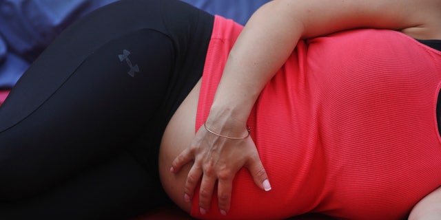A pregnant woman touches her stomach as people practice yoga on the morning of the summer solstice in New York.