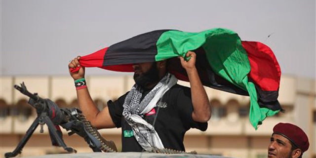 A former rebel fighter holds a pre-Gadhafi's flag at the northern gate of Bani Walid, Libya, Monday, Sept. 19, 2011.