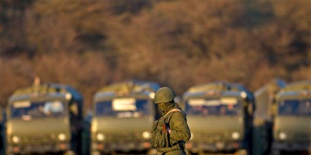 A pro-Russian soldier is backdropped by trucks that define the limits of the pro-Russian troops staging area in the vicinity of an Ukrainian military base in Perevalne, Ukraine, Saturday, March 15, 2014.