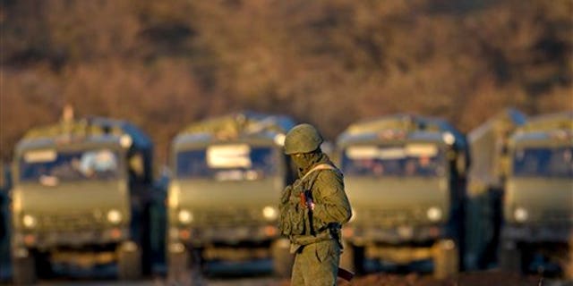 A pro-Russian soldier is backdropped by trucks that define the limits of the pro-Russian troops staging area in the vicinity of an Ukrainian military base in Perevalne, Ukraine, Saturday, March 15, 2014.