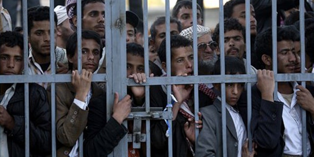 Dec. 24, 2011: Protestors stand behind the gate of a field hospital to watch wounded demonstrators being carried from the site of clashes with security forces, in Sanaa, Yemen.