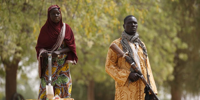 March: A member of a civilian vigilante group holds a hunting rifle while a woman pumps water into jerrycans in Kerawa, Cameroon. Kerawa is on the border with Nigeria and is subject to frequent Boko Haram attacks.