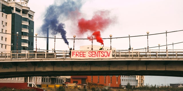 In this handout photo taken on Sunday, Aug. 6, 2017 and released on Monday, Aug. 7, 2017 by Zona.media, Maria Alyokhina and Olga Borisova, members of the Russian punk band Pussy Riot, hold flares and a banner on the bridge nearby outside the prison colony in Yakutsk, Russia, Monday, Aug. 7, 2017.