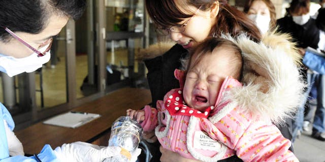 March 17: A baby cries as she is helped by her mother to be screened for radiation exposure before entering an evacuation center in Fukushima, northern Japan. (AP/Kyodo News)