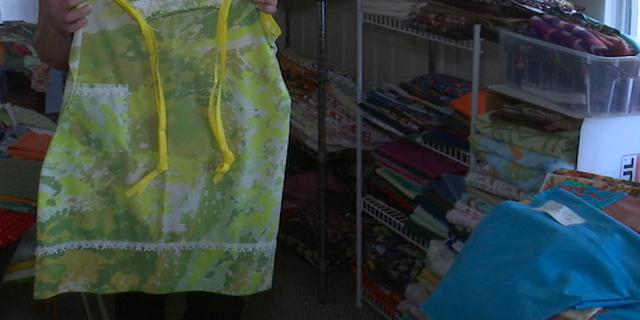 One of the dresses Heft created from a pillowcase in front of shelves holding fabric in a room of her home dedicated to her hobby.
