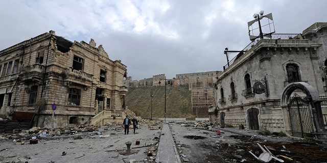 People walk past the old customs buildings (L) and Peoria restaurant (R) near Aleppo's historic citadel, in the government controlled area of the city, Syria December 17, 2016. REUTERS/Omar Sanadiki - RC1A5D700FD0