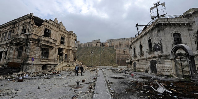People walk past the old customs buildings (L) and Peoria restaurant (R) near Aleppo's historic citadel, in the government controlled area of the city, Syria December 17, 2016. REUTERS/Omar Sanadiki - RC1A5D700FD0