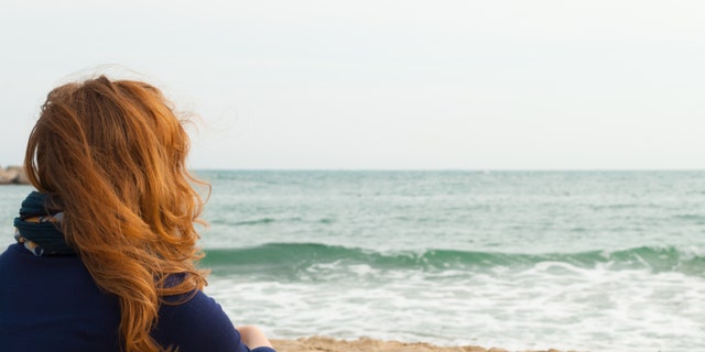 Redhead girl on a Barcelona sand beach looking at the sea, view from behind