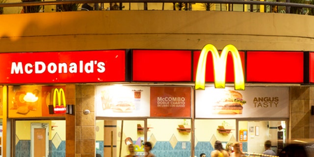 "Palermo, Buenos Aires, Argentina - January 22, 2013: Nighttime view of a McDonald's Restaurant with the light trail of a departing car in the foreground. People can be seen eating inside of the restaurant, entering the restaurant, and walking by on the sidewalk."