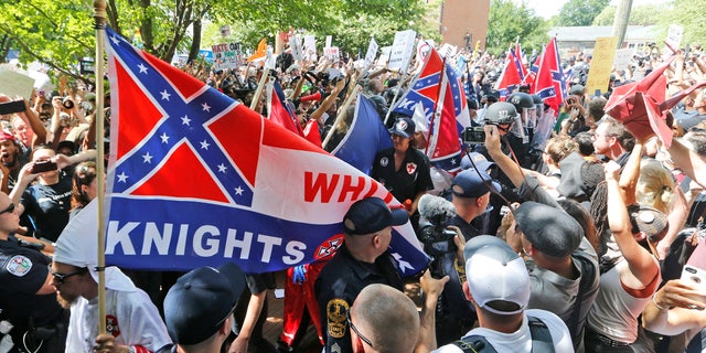 This July 8, 2017 photo shows members of the KKK escorted by police past a large group of protesters during a KKK rally in Charlottesville, Va.