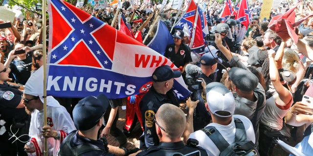 This July 8, 2017 photo shows members of the KKK escorted by police past a large group of protesters during a KKK rally in Charlottesville, Va.