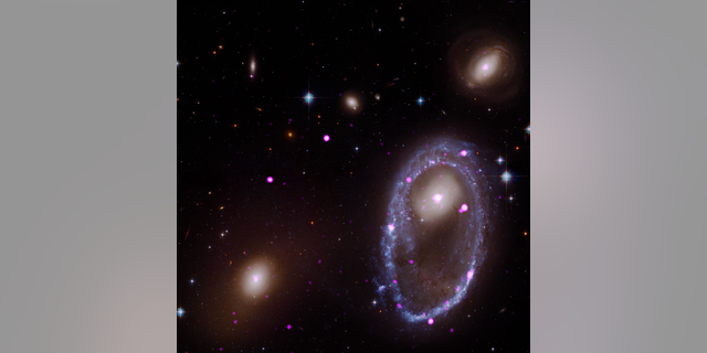 A composite image of the ring galaxy AM 0644-741. The image includes X-ray data from the Chandra X-ray Observatory (purple) and optical data from NASA's Hubble Space Telescope (red, green and blue). The galaxy AM 0644 is located in the lower right.