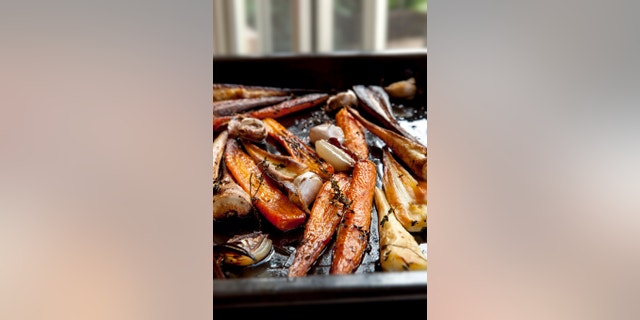 Root vegetables roasting with thyme, garlic and shallots, in baking pan. Carrots and parsnip.