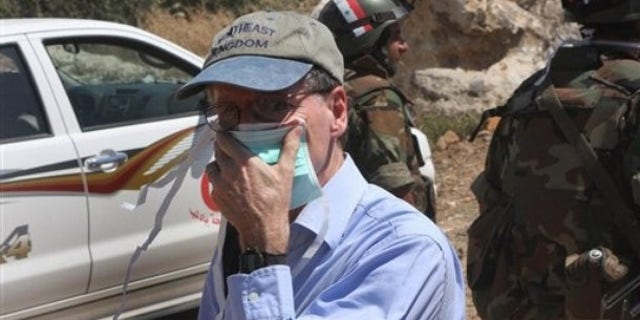 In this photo taken during a government-organized tour for foreign diplomats and the media, US ambassador in Syria Robert Ford, covers his nose from the smell of the dead bodies during his visit with other foreign diplomats to a mass grave, in Jisr el-Shughour, north of Syria, on Monday, June 20, 2011.