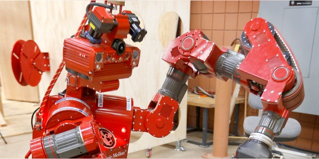 In this Wednesday, Dec. 11, 2013 photo, the CMU Highly Intelligent Mobile Platform robot, known as CHIMP, (CMU Highly Intelligent Mobile Platform) is put through some paces as it is switching the hold of a fire hose from one grasping unit to another at the National Robotics Engineering Center in Pittsburgh. Carnegie Mellon researchers are testing the new search-and-rescue robot that will compete in the U.S. Defense Department's upcoming national robotics competition in Florida. Competitors from other schools and companies will be vying for a $2 million U.S. Defense Department prize. (AP Photo/Keith Srakocic)