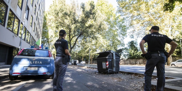 Police officers stand near the site where a trash bin was removed after two amputated legs were found in Rome.