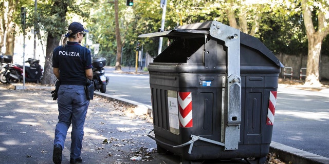 An Italian police officer walks past the site where a trash bin was removed after two amputated legs were found.