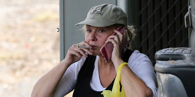 The visibly stressed Roseanne is seen sitting on a curb in a hat, cuffed jeans and flip flops talking a phone call while smoking a cigarette.
