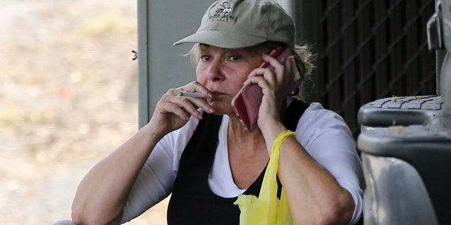 The visibly stressed Roseanne is seen sitting on a curb in a hat, cuffed jeans and flip flops talking a phone call while smoking a cigarette.