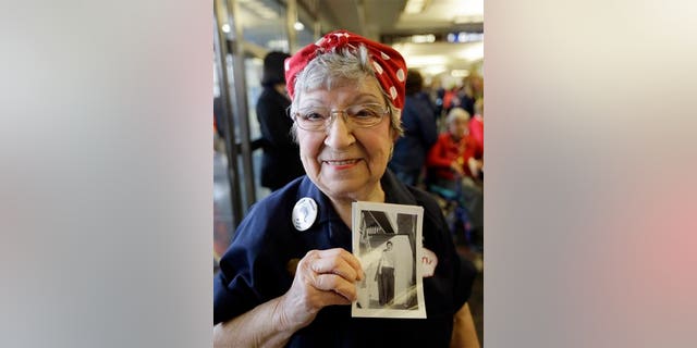 Former Rosie, T. Ogden of Aurora, Ill. shows a photo of herself after greeting fellow Rosies from Michigan on their arrival at the Ronald Reagan Washington National Airport, Tuesday, March 22, 2016 in Washington. Seven decades after their "we can do it" attitude proved invaluable to the Allied victory in World War II, some "Rosie the Riveters" are being honored with a flight to Washington, D.C. The women will check out the National World War II Memorial and Arlington National Cemetery, and have lunch with members of Congress. (AP Photo/Carlos Osorio)