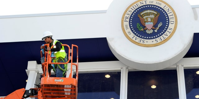 Workers use a hydraulic lift to position themselves to clean the bullet-proof glass under the Seal of the President on the inaugural reviewing stand in front of the White House in Washington January 12, 2013. U.S. President Barack Obama, family and dignitaries will watch the parade from the stand, after the Presidential Inauguration on January 21, 2013. REUTERS/Mike Theiler (UNITED STATES - Tags: POLITICS) - RTR3CD6F