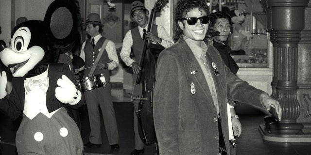 Mickey Mouse follows Michael Jackson as he strolls at a shopping street at the Tokyo Disneyland during his sightseeing tour September 29, 1987.