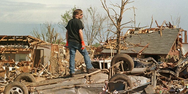 A man stands atop a smashed car in a tornado-ravaged neighborhood south of Oklahoma City. The F5 tornado killed some 44 people in May 1999.