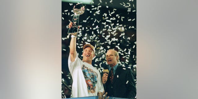 John Elway holds up the Vince Lombardi Trophy as he is interviewed by former Steelers quarterback and broadcaster Terry Bradshaw after leading his Denver Broncos team to a second consecutive Super Bowl victory, January 31