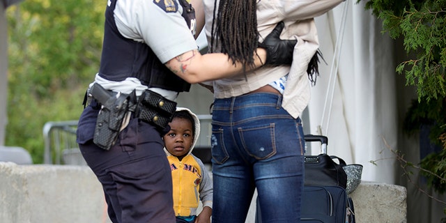 Evanston, whose family stated they are from Haiti, watches as a Royal Canadian Mounted Police officer pats down his mother.