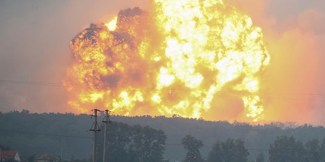 Smoke and flames rise over a warehouse storing ammunition for multiple rocket launcher systems at a military base.