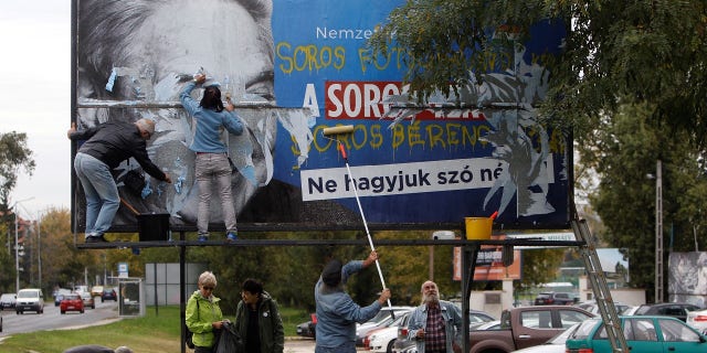 Activists remove a government billboard displaying George Soros in monochrome next to a message urging Hungarians to take part in a national consultation about what it calls a plan by the Hungarian-born financier to settle a million migrants in Europe per year.