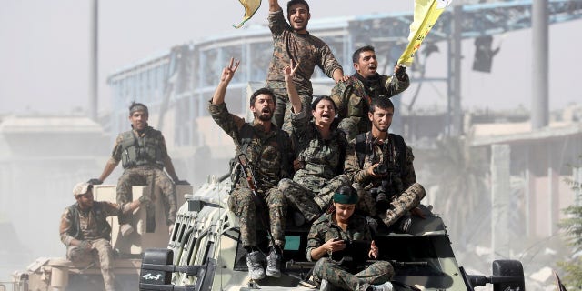 SDF fighters ride atop military vehicles as they celebrate victory in Raqqa, Syria.