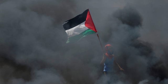 FILE -- A boy holds a Palestinian flag as he stands amidst smoke during a protest against U.S. embassy move to Jerusalem.