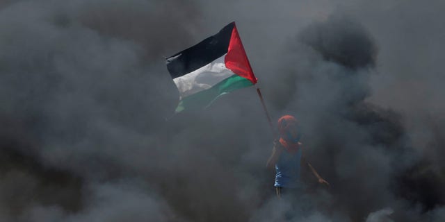 FILE -- A boy holds a Palestinian flag as he stands amidst smoke during a protest against U.S. embassy move to Jerusalem.