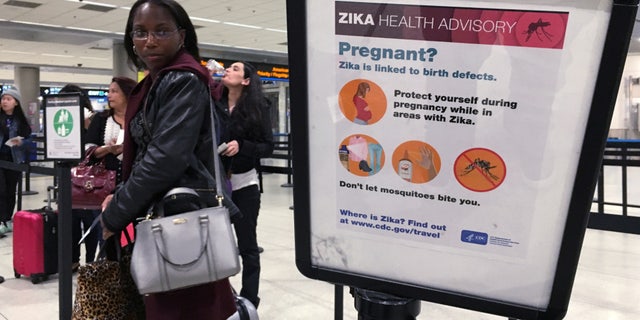 A woman looks at a Center for Disease Control (CDC) health advisory sign about the dangers of the Zika virus as she lines up for a security screening at Miami International Airport in Miami, Florida, U.S., May 23, 2016.