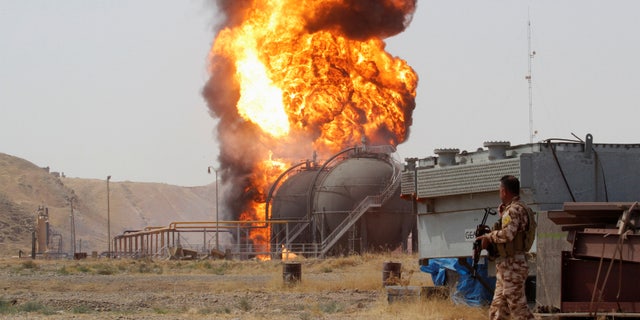 A member of the Kurdish Peshmerga forces walks as smoke rises after an attack at Bai Hassan oil station, northwest of Kirkuk, Iraq, July 31, 2016.
