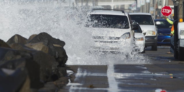 Drivers make their way along a beach road as a wave crashes onto the street due to a combination of high tides and high surf in Oceanside, California October 27, 2015.