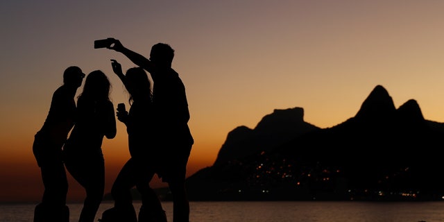 People take selfies during sunset on the rocks of Arpoador beach in Rio de Janeiro, Brazil July 4, 2016.