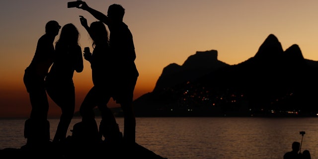 People take selfies during sunset on the rocks of Arpoador beach in Rio de Janeiro, Brazil July 4, 2016.