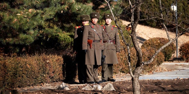 North Korean soldiers looking toward the South at the DMZ. South Korea is reportedly broadcasting news about the defector through loudspeakers.