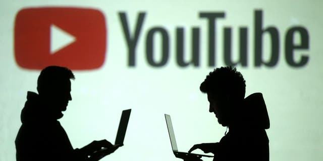 Silhouettes of mobile device users are seen next to a screen projection of Youtube logo in this picture illustration taken March 28, 2018. REUTERS/Dado Ruvic/Illustration - RC1502FFC0B0
